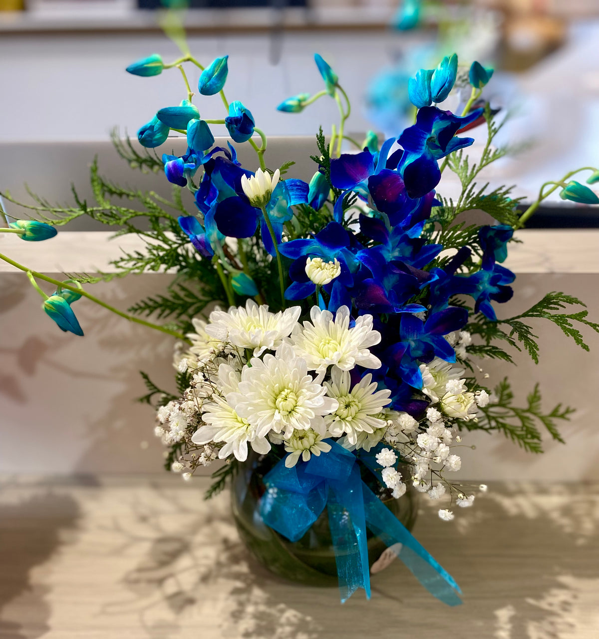 Blue Singapore orchids paired with white chrysanthemums and seasonal foliage arranged in a clear glass vase