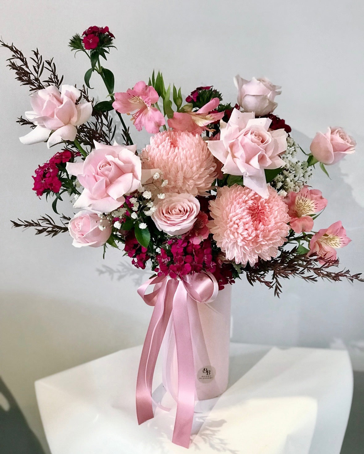 Cylinder pink ceramic vase featuring blush roses and chrysanthemum mums as the main blooms, complemented by soft pastel seasonal flowers.