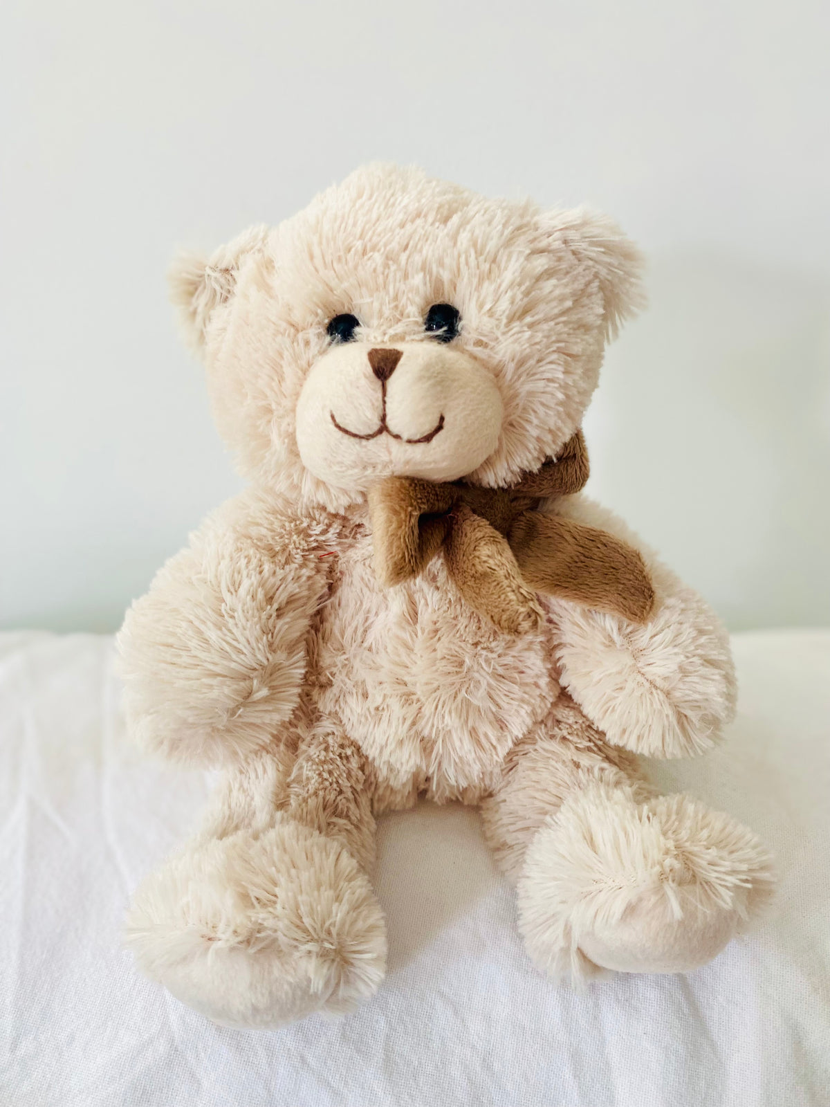 Soft beige plush teddy bear featuring a classic brown bow, approx. 24cm tall.
