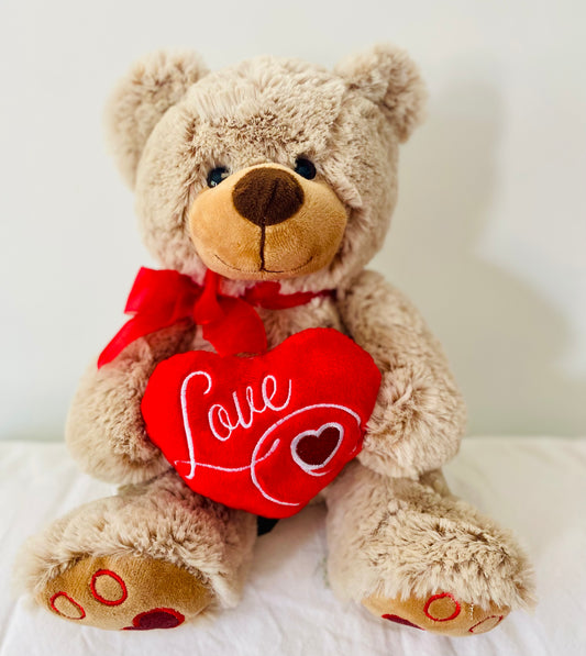 Soft beige plush teddy bear holding a red ‘Love’ heart, approx. 26cm tall.