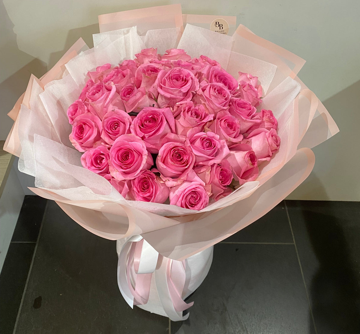 24 premium long‑stem pink roses arranged in a lush bouquet with soft complementary foliage and elegant wrapping.