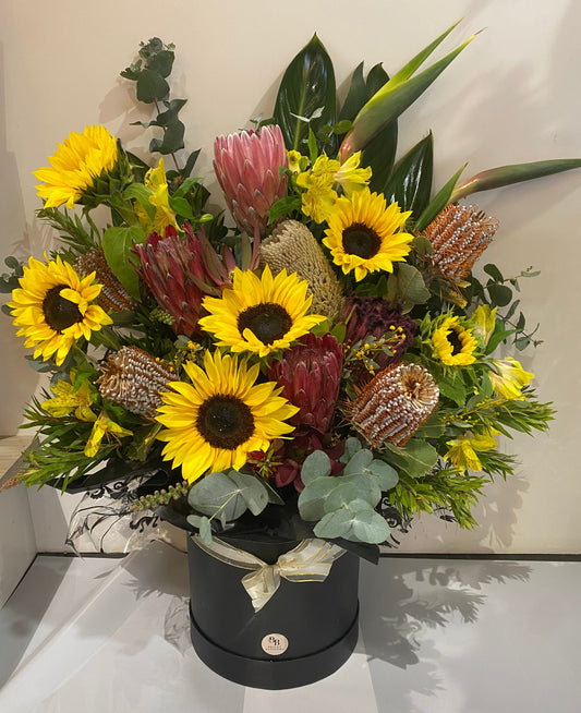 Sunflower & Natives – Premium Hatbox featuring bright sunflowers arranged with seasonal native blooms including proteas and banksias in a premium round hatbox