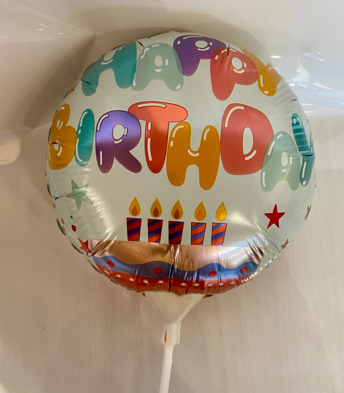 Round Happy Birthday foil balloon with colourful cake illustration, approx. 22cm in diameter.
