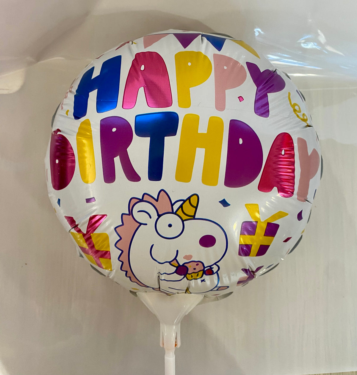 Round Happy Birthday foil balloon featuring a colourful unicorn design, approx. 22cm in diameter.