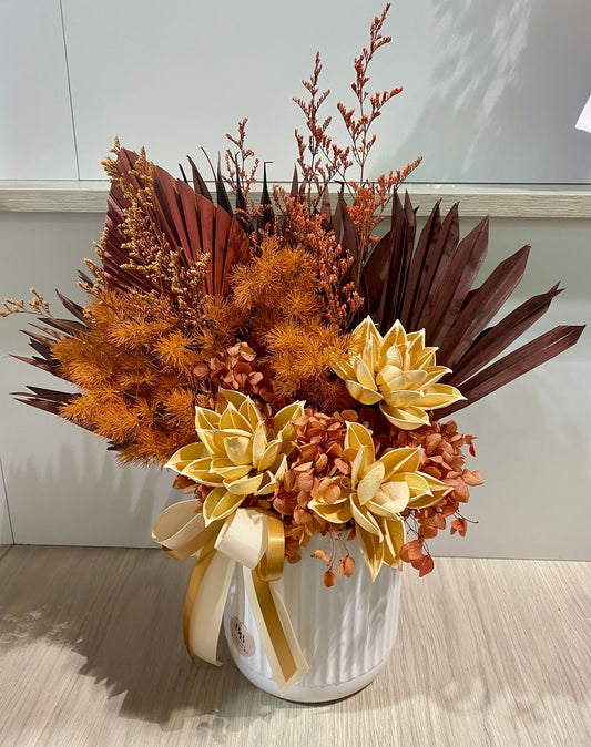 Rustic dried and preserved flower arrangement in warm orange and brown tones displayed in a modern vase, featuring natural textures and long‑lasting blooms