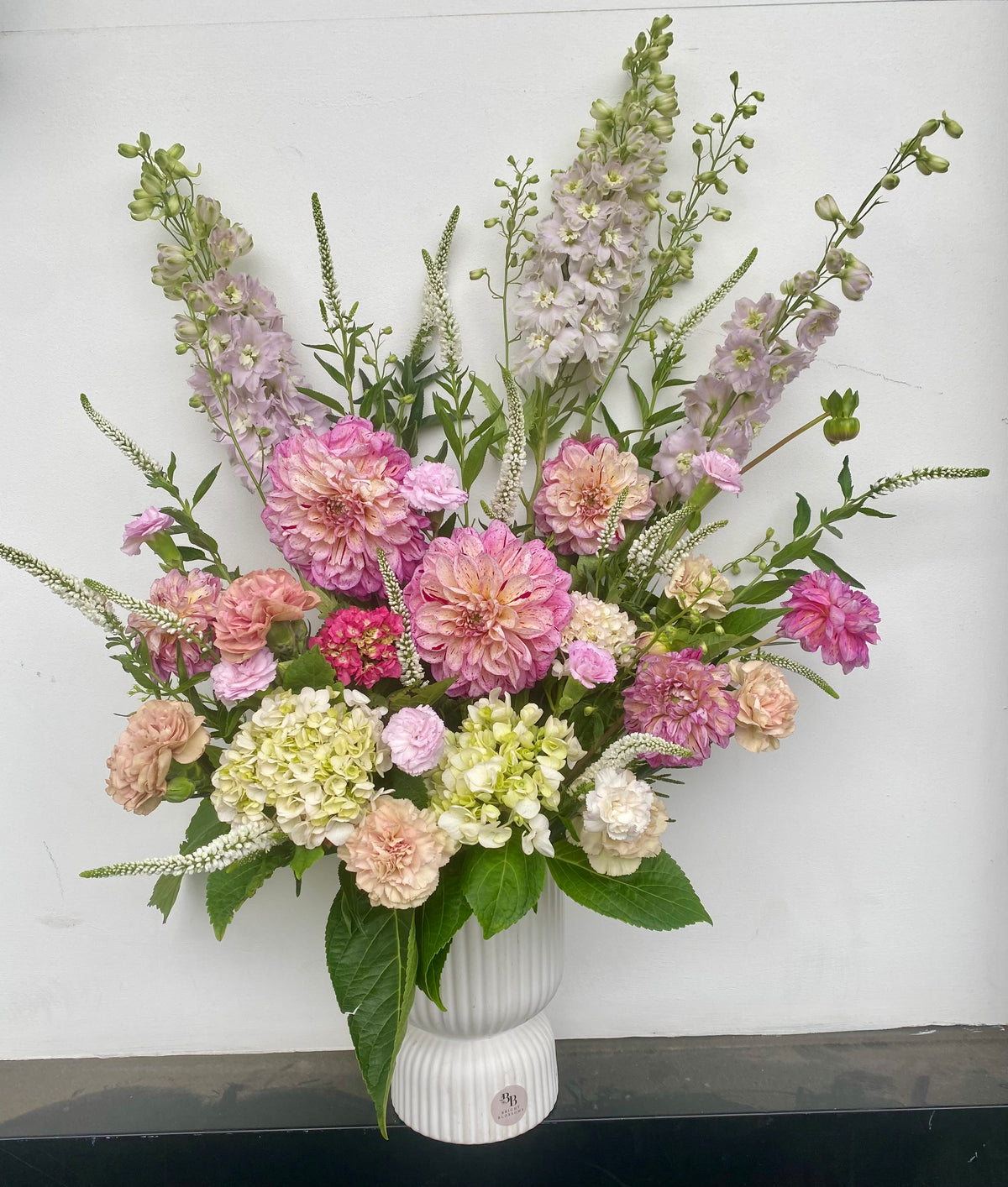Pastel Grace Vase featuring tall pastel blooms including delphiniums, hydrangeas, dahlias and carnation sims arranged in a modern ribbed ceramic vase.