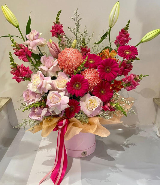 Signature Bloom Hatbox featuring chrysanthemum mums, gerberas, roses, oriental lilies and snapdragons arranged in a premium round hatbox.
